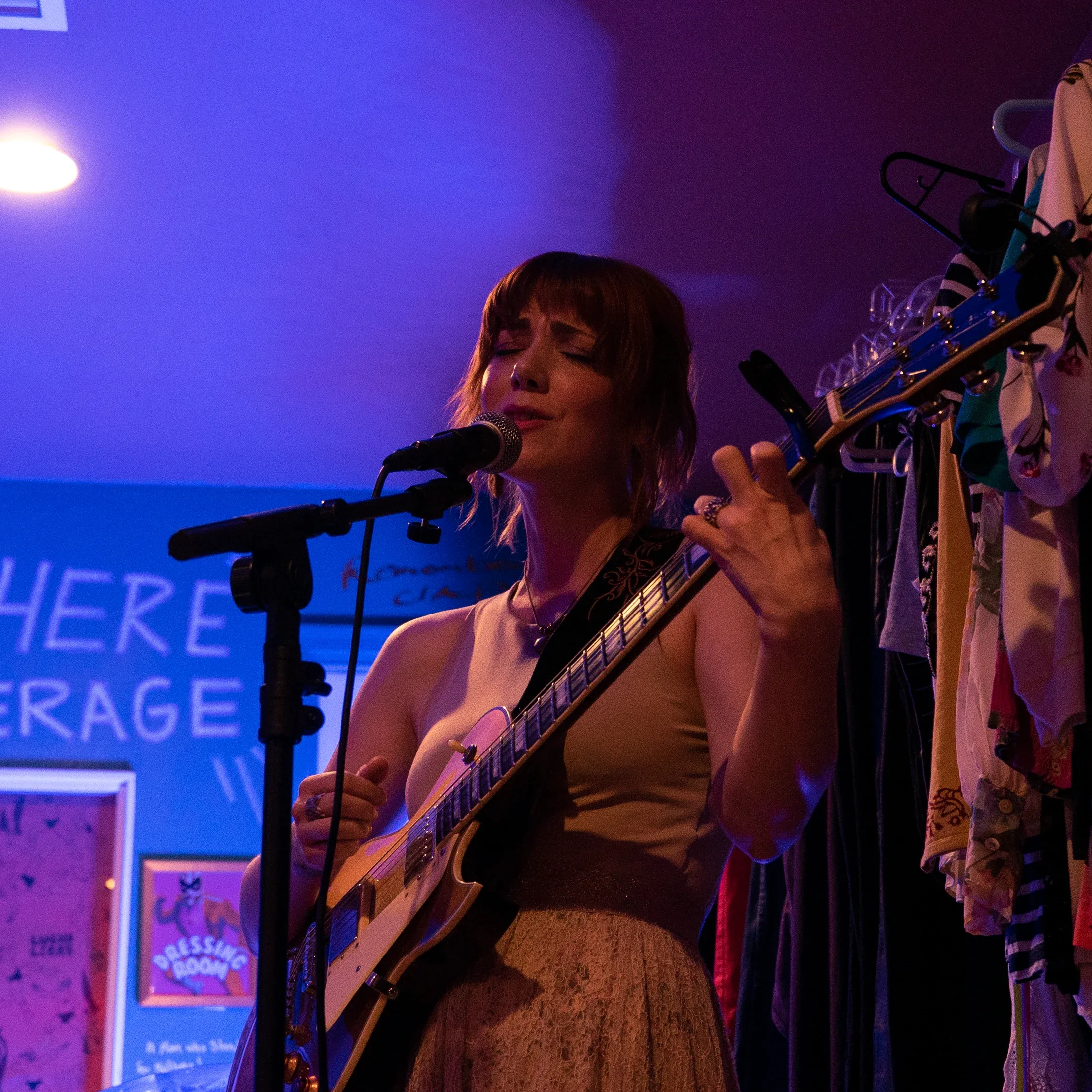 Bree Cole singing and playing electric guitar in blue and purple light