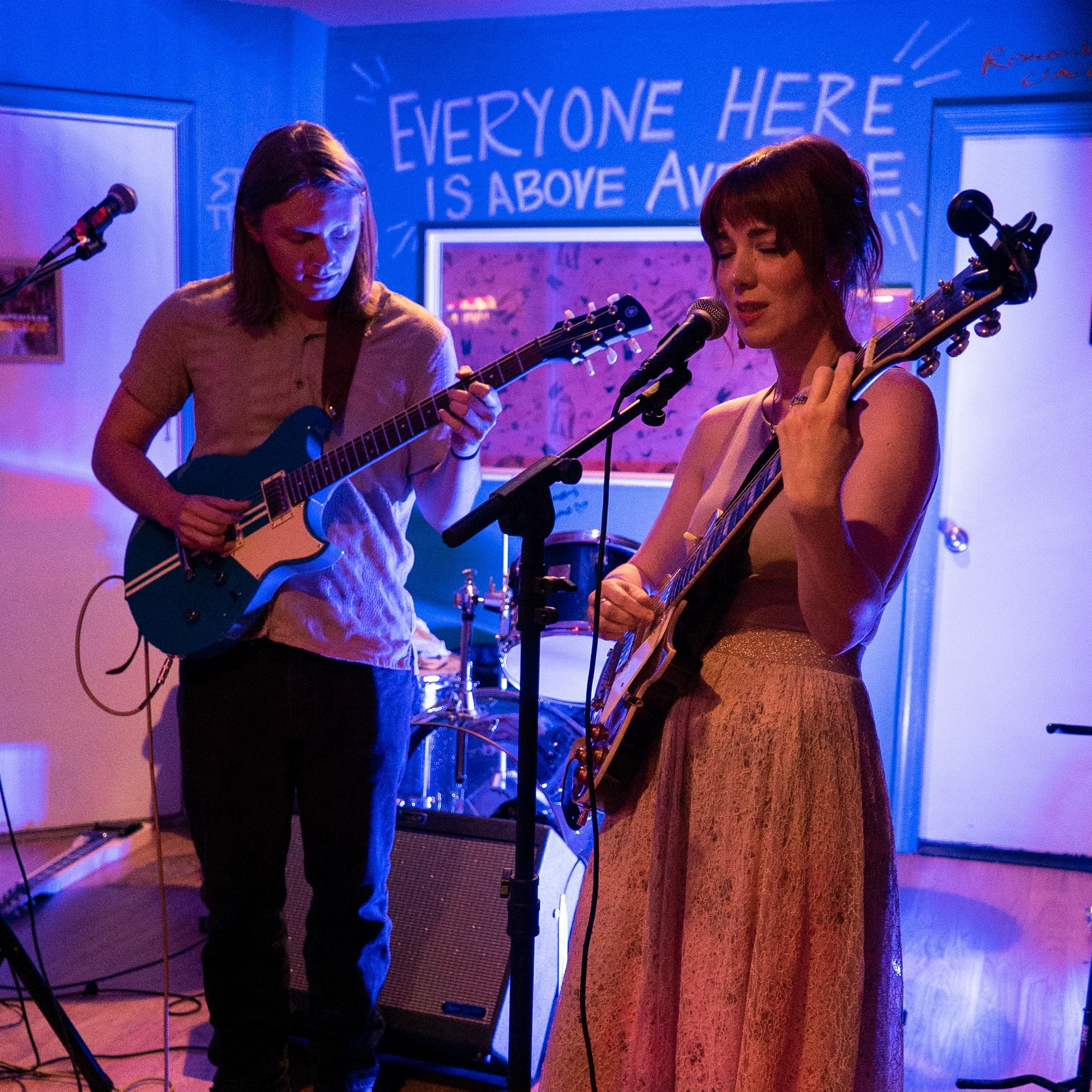 Bree Cole performing electric guitar with another guitarist in a colorful room